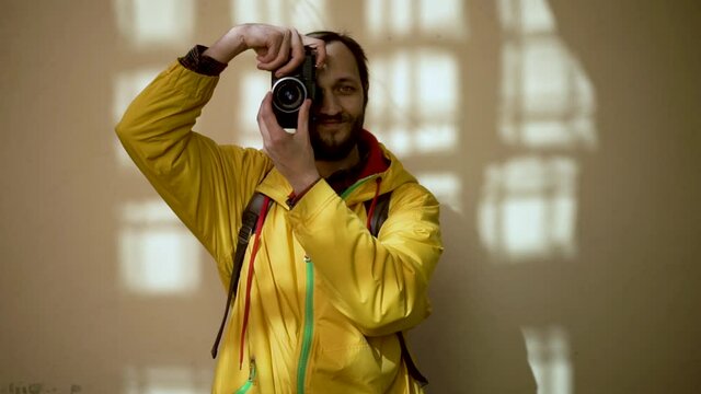 Adult male tourist photographer in yellow jacket looking into the camera and taking photos with old film camera. Male backpacker with film camera traveling at the ancient city