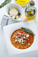 Risotto with sun dried tomato pesto and belper knolle, elevated view on a white stone background, vertical shot