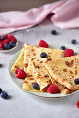 Pancakes with raspberries and blueberries on a plate, on a gray background, side view.