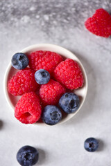 Raspberries, blueberries on a saucer, on a gray background, close-up, top view.