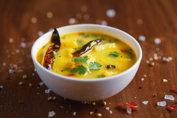 Close-up of healthy curry of yogurt (curd) and potato (Dahi Aloo or Aaloo ) an Indian Classical dish,  served in a white ceramic bowl. Over Wooden Background with red chilies and salt. Top view.