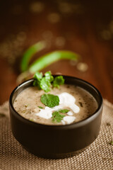 Close-up of Methi-Matar-Malai with white curry with fresh green chilies, mint leaves, and onions. A popular, delicious Indian recipe in a black bowl over wooden background.