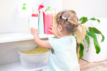 Toddler touches bottles of household chemicals, household cleaning products. - obrazy, fototapety, plakaty