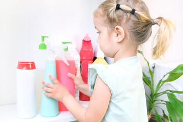 Toddler touches bottles of household chemicals, household cleaning products.