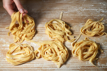 Woman's hands make tagliatelle or fettuccine on pastry board. Fresh egg pasta nests.