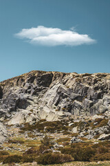 Top of a mountain seen from below with a large cloud in the sky.