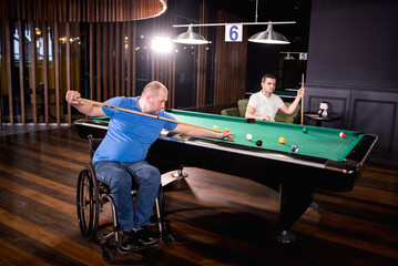 Adult men with disabilities in a wheelchair play billiards in the club