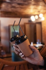 Girl holding coffee on a beautiful background. The concept of the beginning of the morning, vigor and environmental friendliness. Paper cup with takeaway coffee in hand. Vertical photo