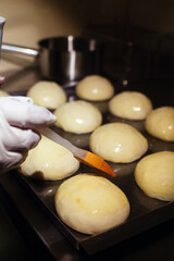 The baker greases the buns before placing them in the oven. Home baking and confectionery production. Home cooking concept. Vertical photo