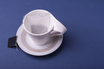 Closeup shot of a single teabag inside a porcelain white cup on dark blue background © Masoud Rezaeipoor/Wirestock