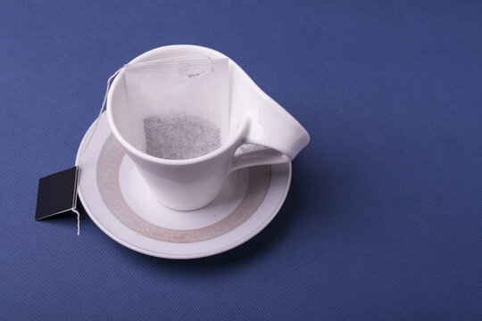 Closeup shot of a single teabag inside a porcelain white cup on dark blue background