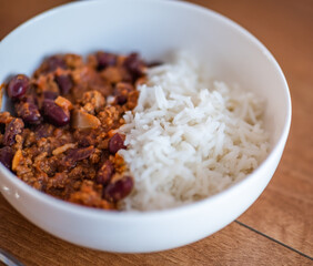 Close up and selective focus of meat chilli concarne and white rice in a white bowl on a wooden surface with intentional shallow depth of field and bokeh