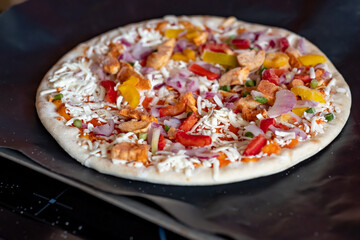 Close and selective focus of a readymade frozen stone baked thin sweet chilli chicken pizza on a baking mat ready to be cooked in the oven for Saturday night dinner