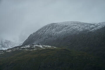 Minimalist gloomy highlands landscape with snow-capped high mountains in overcast weather....