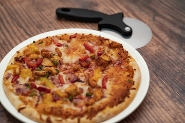 Close up and selective focus of a home cooked thin crust sweet chilli chicken pizza on a white plate on a wooden table