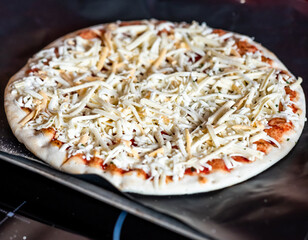 Close and selective focus of a readymade frozen stone baked thin four cheese pizza on a baking mat ready to be cooked in the oven for Saturday night dinner