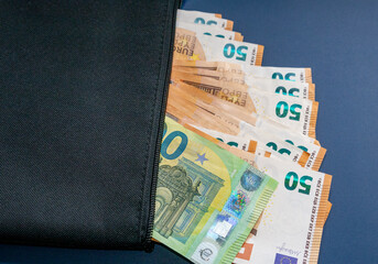 Schwarze Geldtasche mit einem Hundert Euro Schein und mehreren Fünfzig Euro Banknote, vor blauen...