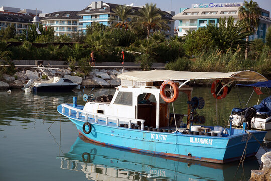 Side / Turkey - October 16 2019: A small blue and white boat stands in a bay near the hotels. A fishing boat awaits its owner on the river. Amazing vacation in Turkey.