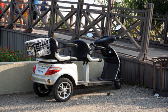 Side / Turkey - October 16 2019: A cute little three-wheeled electric car is parked near a bridge over a river. Convenient inexpensive eco-friendly transportation for travelers.