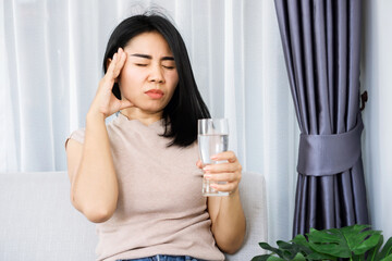 Asian woman suffering from headache after drinking cold water hand holding her head and glass of water