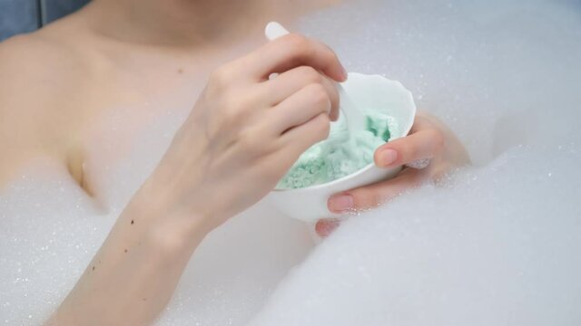 Young woman is preparing mixing alginate mask lying in bathroom with foam at home, bowl closeup. Spa beauty treatment, procedure. Female wellness, skincare and self love concept.
