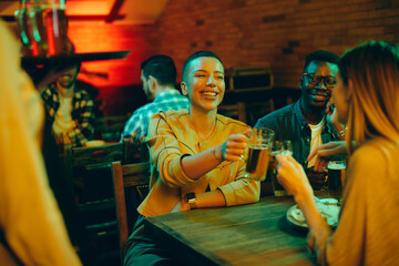 Happy African American woman toasting with her friends while drinking beer in a bar.