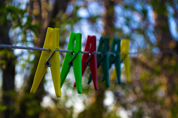 Multi-colored plastic clothespins. Royalty-free high quality stock photo of a plastic clothespin attached to a clothesline outdoors. Green garden background - obrazy, fototapety, plakaty