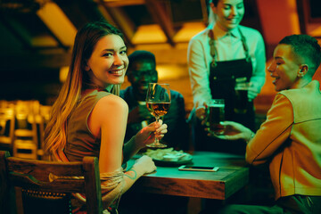 Young smiling woman having glass of wine while enjoying with friends in a bar at night.