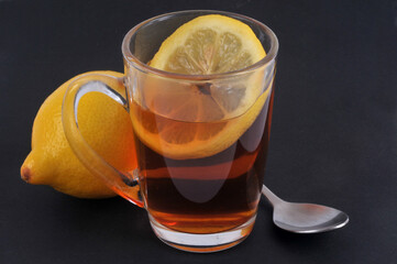 Mug de thé au citron avec une rondelle de citron à co^té d'un citron jaune et une cuillère en gros plan sur fond noir