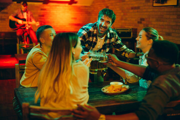 Happy friends toasting with beer and having fun while gathering in a bar at night.