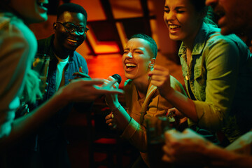 Group of happy friends singing karaoke during a night party at the pub. - Powered by Adobe