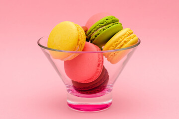 several color macaron cakes in a glass vase on a pink background