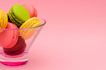 several multicolor macaron cakes in a glass vase on a pink background