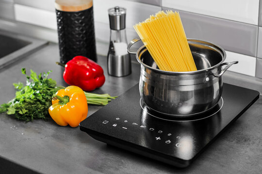 Italian spaghetti in a pan on an induction stove. vegetables and greens on the kitchen table