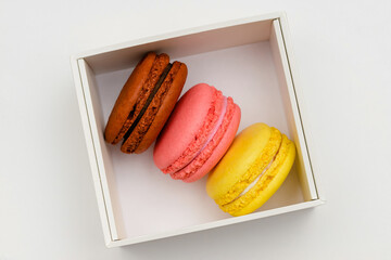 three color macaron cakes in a white box on a white background