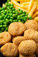 Fried crispy chicken nuggets with ketchup, french fries and green peas in black plate