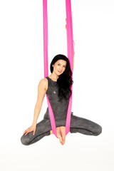 Beautiful gymnast does fly yoga on pink hammock. She smiling and looking straight.