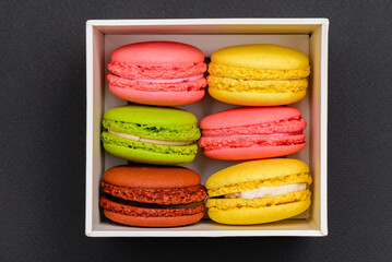 six multicolored macaron cakes in a white cardboard box on a black background