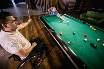 Adult men with disabilities in a wheelchair play billiards in the club