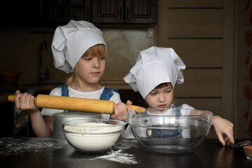 little girls sisters in chef's hats preparing to knead the dough, children are cooking