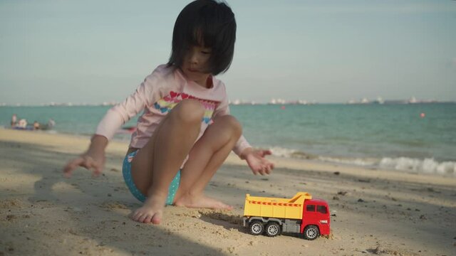 Asian chinese girl child playing with earth mover toys by the beach