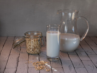 glass jug and a glass of oat milk on the table with a jar of oatmeal