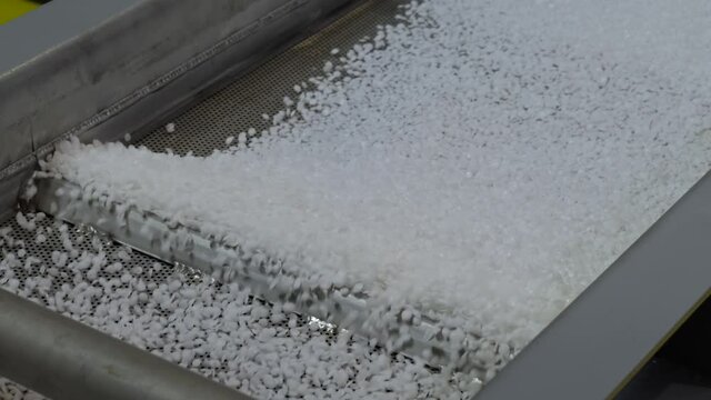 Waste plastic recycling machine: recycled plastic granules - propylene or polyethylene pellets on shale shaker, conveyor belt - close up. Separation, ecology, automated technology concept
