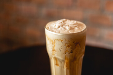 Ice coffee and caramel on a wood table with brick wall background.