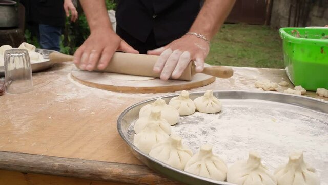 hands cooking Georgian traditional dish Khinkali meat. outside village cuisine. Video footage. Two men  in process of cooking a national famous food make dumplings from dough and fill them with meat