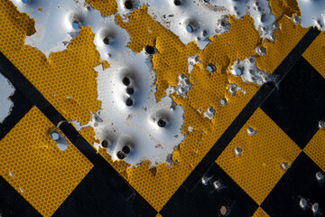 Close-up of checkered road sign with bullet and shotgun holes.
