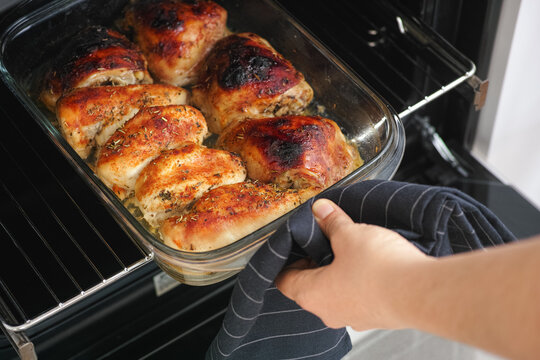 A woman taking a tray with cooked chicken breasts out of an oven