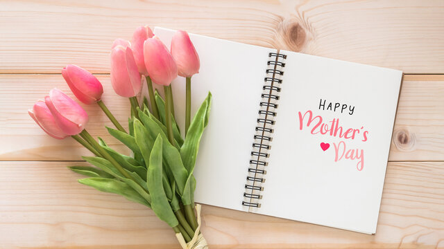 Happy Mother’s Day holiday greeting celebration on white note book page background with tulip flower on wood backdrop