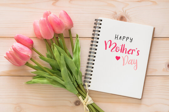 Happy Mother’s Day holiday greeting celebration on white note book page background with with tulip flower gift for mom on wood backdrop