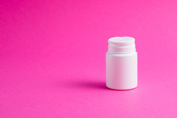 White jar of pills or vitamins on a pink paper background. Medicine on background with copy space.